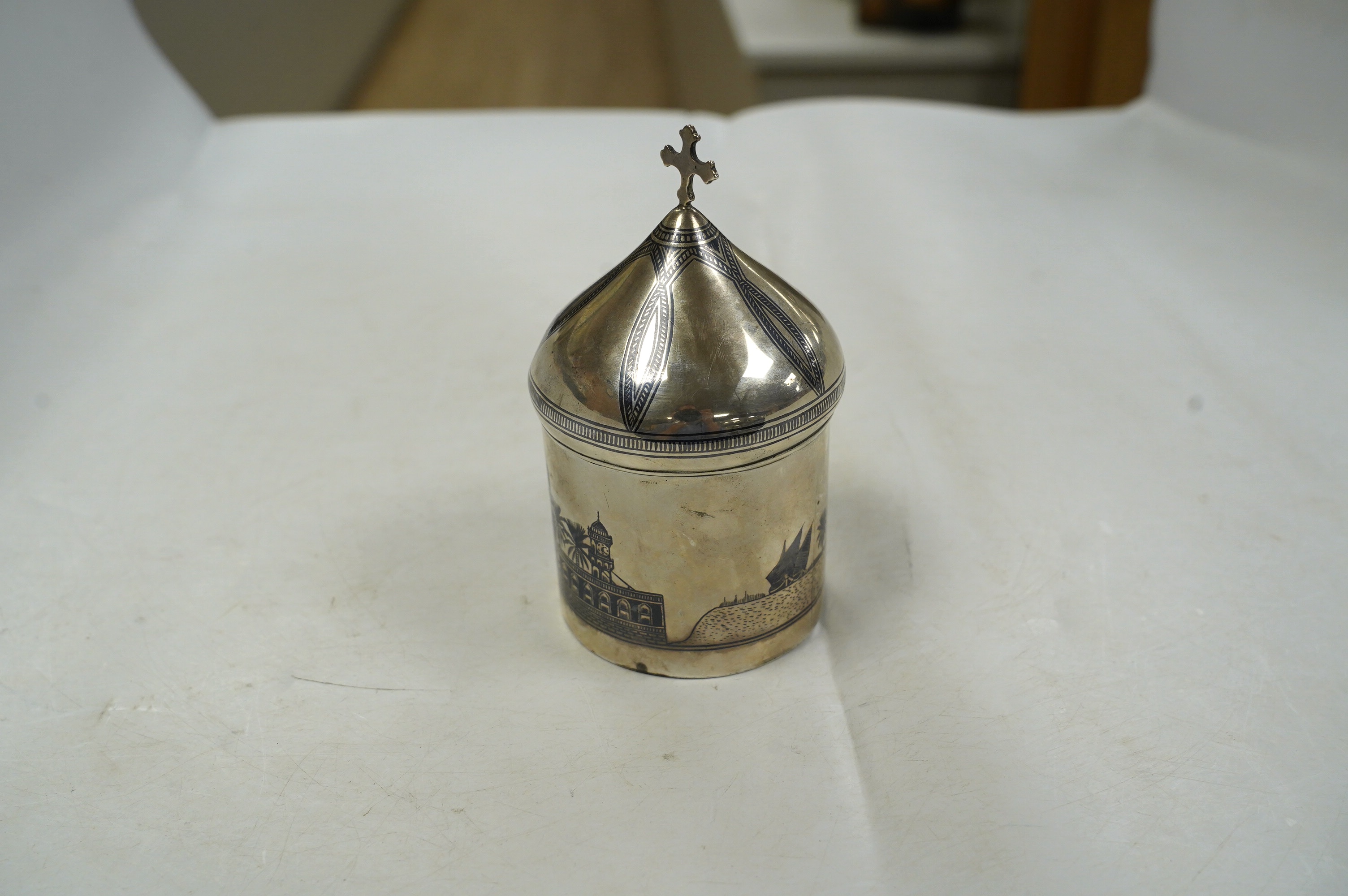 A Middle Eastern white metal and niello box and cover, with cross finial, 11.8cm, gross weight 4.4oz. Condition - poor to fair